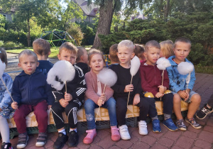 Kilkoro dzieci z grupy Ważki siedzą na ławce w ogrodzie z watą cukrową