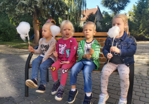 Czworo dzieci z grupy Ważki siedzą na ławce w ogrodzie z watą cukrową