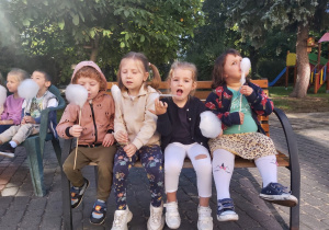 Czworo dzieci z grupy Ważki siedzą na ławce w ogrodzie z watą cukrową