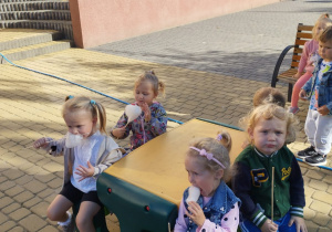 Czworo dzieci z grupy Biedronki siedzą z watą cukrową w ogrodzie przy stoliku