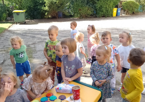 Kilkoro dzieci z grupy Biedronki stoi przy stoliku, przy którym mają malowane buzie
