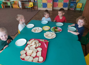 Kilkoro dzieci siedzi przy stoliku z naszykowanymi produktami na kanapki