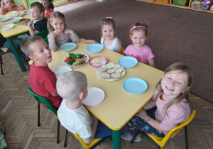 Kilkoro dzieci siedzi przy stoliku z naszykowanymi produktami na kanapki