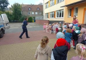 Dzieci z grupy Biedronki i Ważki stoją na placu przedszkolnym i pani polocjantka