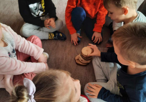 Kilkoro dzieci na dywanie ogląda plastry drewna