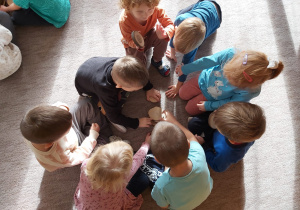 Kilkoro dzieci segreguje na dywanie plastry drewna