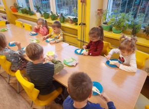 Dzieci przy stole układają na pieczywie ser i szynkę