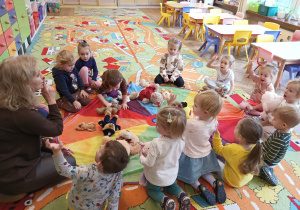 Dzieci siedzą wokół chusty, na której leżą misie