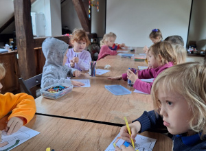 Dzieci siedzą przy stole i kolorują pracę plastyczną