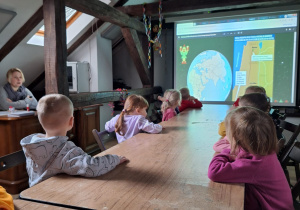 Dzieci siedzą przy stole i oglądają prezentację na rzutniku