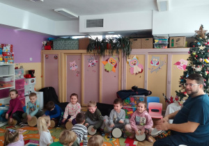 Siedmioro dzieci z grupy Motylki i gość grają na bebnach