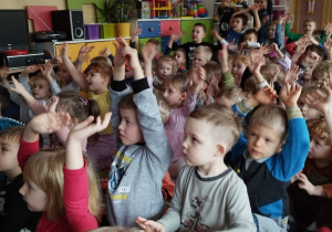 Dzieci siedzą na dywanie i podnoszą ręce w górę