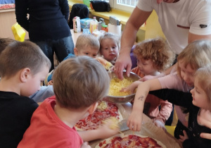 Dzieci posypują pizze tartym serem