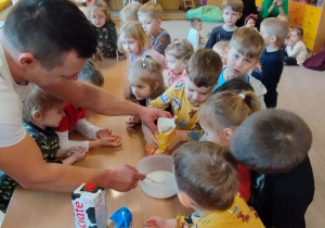 Pan Tomasz pomaga dzieciom wsypywać mąkę do miski