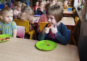 Pawełek, Kaja i inne dzieci z grupy Biedronki przy stolikach jedzą pizzę