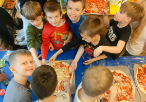 Chłopcy z grupy Motylki posypują pizze serem