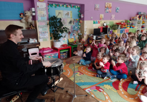 Dzieci słuchają, jak pan Piotr gra na perkusji
