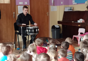 Pan Piotr gra na perkusji, a dzieci siedząna dywanie