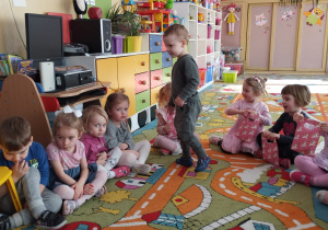dzieci siedzą na dywanie, Tymon wręcza dziewczynkom upominki