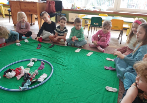 Dzieci z grupy Ważki siedzi na dywanie, przed każdym leży skarpetka, a na środku obręcz ze skarpetkamina dłoniach mają one skarpetki