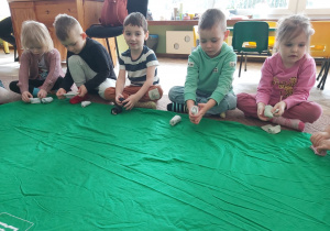 Kilkoro dzieci z grupy Ważki siedzi na dywanie i składają skarpetki