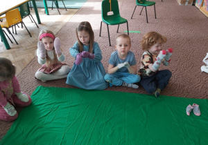 Kilkoro dzieci z grupy Ważki siedzi na dywanie, na dłoniach mają założone skarpetki