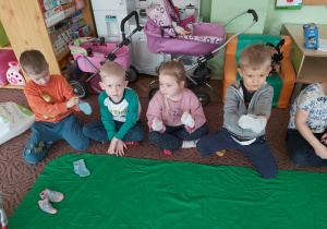 Kilkoro dzieci z grupy Ważki siedzi na dywanie, na dłoniach mają założone skarpetki