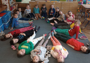 Dzieci z grupy Motylki siedzą i leżą na dywanie pokazując swoje skarpetki