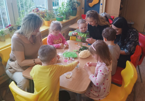 Dzieci z mamami przy stoliku ozdabiają jajka