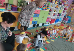 Dzieci siedząc na dywanie układają na kartonikach sylwety pisanek