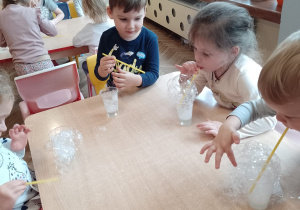 Adaś, Sofiia, Pawełek siedzą przy stoliku i robią bańki mydlane w kubeczkach