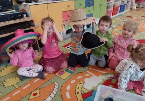 Emilka, Lenka, Pawełek, Filipek i Stenia siedzą na dywanie podczas zabawy z kapeluszami