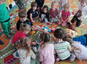 Dzieci siedzą na dywanie i patrzą na różne odpady-śmieci