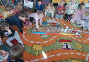Dzieci siedza na dywanie, a Pola ustawia w pudełku sylwetę urządzenia