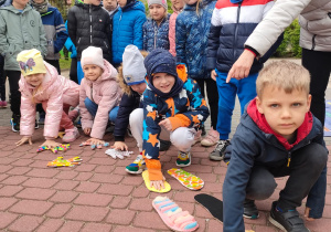 Kilkoro dzieci kuca i trzyma ręce na sylwetach dłoni i stóp