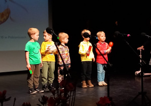 Pięciu chłopców z instrumentami w ręku stoi na scenie, a dziewczynka stoi z boku z panią Małgosią