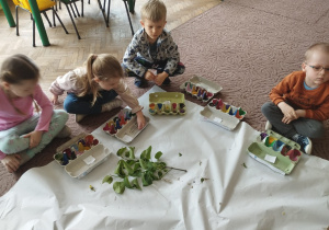 Kilkoro dzieci siedzi na dywanie z pomalowanymi pudełkami na skarby