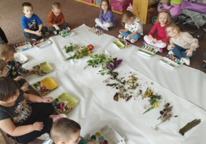 Dzieci siedzą na dywanie z pomalowanymi pudełkami na skarby wokół rozłożonych skarbów przyrody