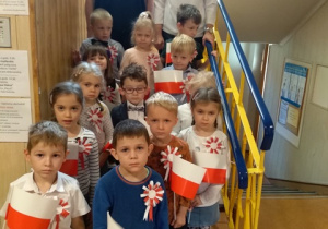 Panie i dzieci z grupy IV z flagami pozują do zdjęcia na schodach przedszkolnych