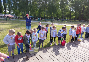 Dzieci stoją obok siebie, a wybrane napełniają rurki wodą