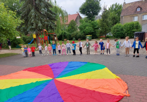 Dzieci trzymają się za ręce, przed nimi leży chusta animacyjna