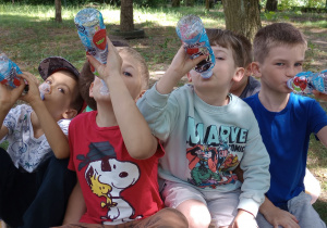 Kilku chłopców z grupy Motylki siedząna kocu i piją napój z butelki