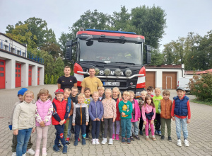 Wspólne zdjęcie dzieci z grupy Mrówki z dwoma strażakami przy wozie strażackim