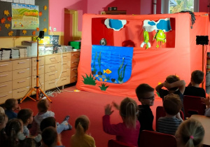 Dzieci siedzą na dywanie i oglądają przedstawienie