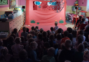 Dzieci siedzą na dywanie i oglądają przedstawienie