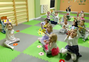 Dzieci siedza i unoszą w dłoniach sylwety motyli