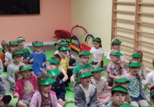Dzieci siedzą w zielonych daszkach na głowach podczas koncertu