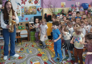 Pani muzyk gra na saksofonie, a dzieci poruszają się do muzyki