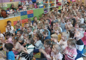 Dzieci siedzą na dywanie i klaszczą w dłonie