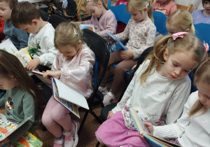 Dzieci siedzą w czytelni i oglądają książki